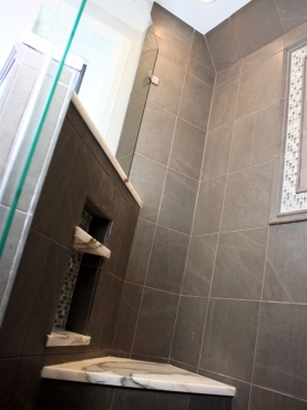 A custom-cut glass shower enclosure makes the shower appear larger while the stone and glass mosaic tile and Calacatta marble accents brighten the space.